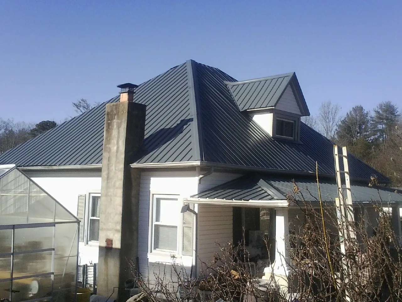 Dark blue standing seam metal roof on a white farmhouse with dormer — Slate & Tile Roof Repair by Roofing Brothers in Camp Lejeune
