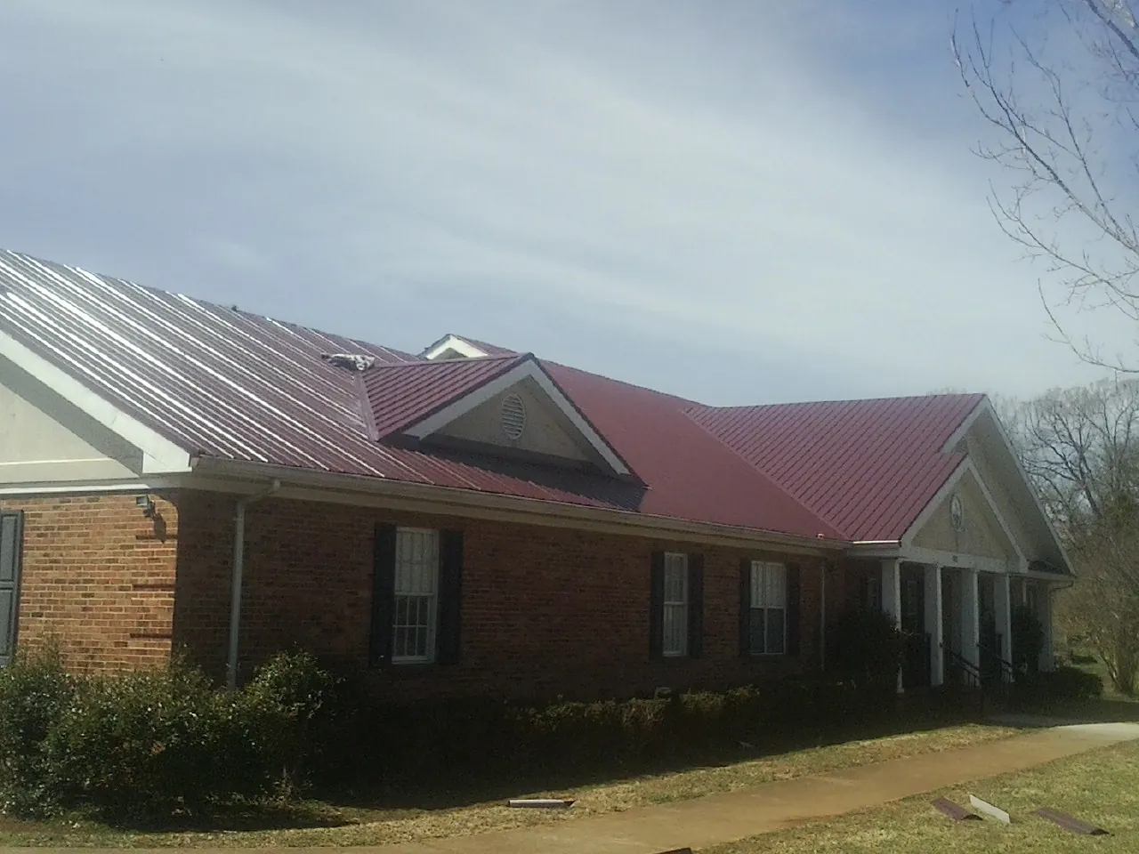 Red metal roof with gabled entries on a long brick building, from a Hail Damage Roof Repair job in Camp Lejeune
