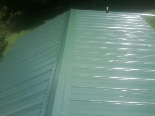 New green metal panels meeting at the ridge of a roof — Flat Roof Repair work by our crew in Camp Lejeune
