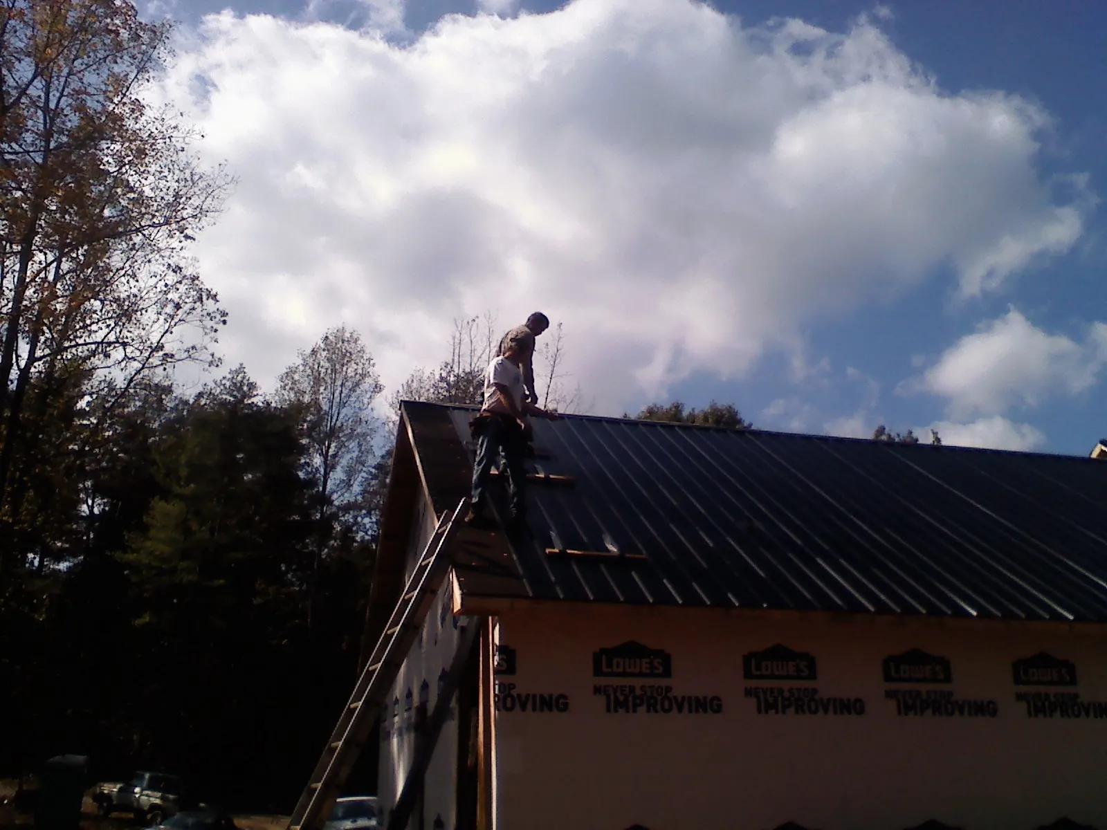 Roofer fastening dark metal panels high against a cloudy sky, from a Roof Inspection job in Camp Lejeune