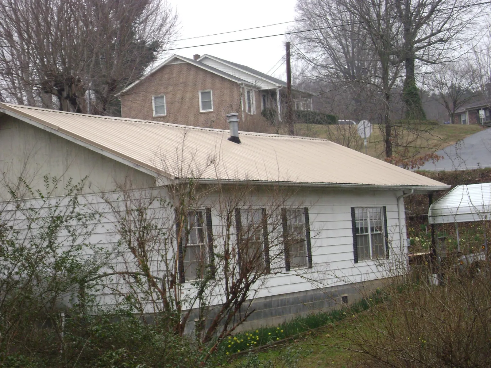 Tan metal roof on a white sided house set into a hillside — Commercial Roofing by Roofing Brothers in Camp Lejeune