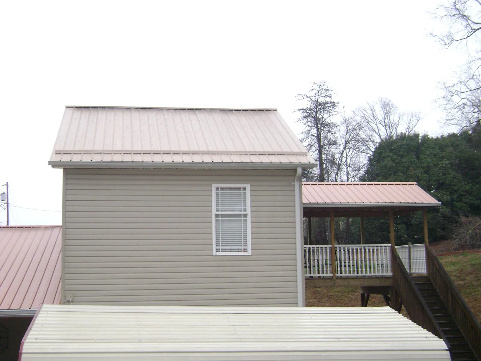 Tan metal roofs on a two story addition and attached porch, from a Roof Replacement job in Camp Lejeune